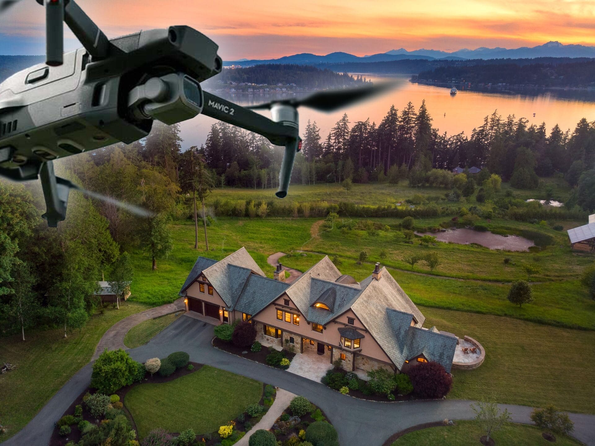 A drone flies over a large, picturesque house surrounded by well-manicured lawns and lush green trees. As part of luxury real estate marketing, the sun sets, casting a warm glow over a serene lake and forested landscape in the background.