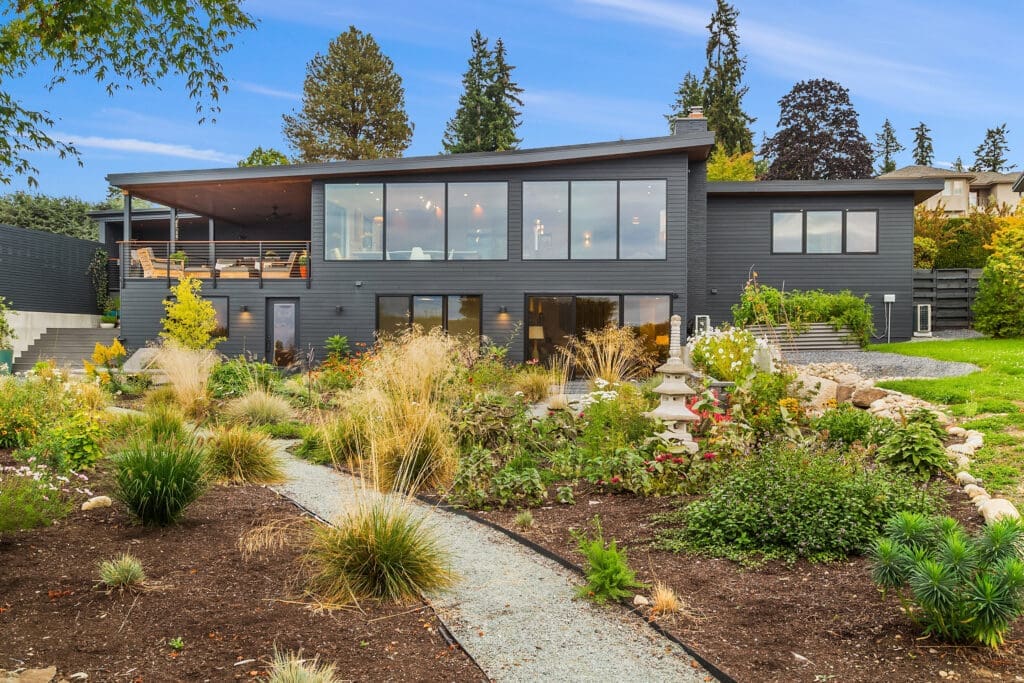 Finding a real estate photographer near you. Modern exterior of a stylish home surrounded by lush landscaping in the Pacific Northwest, featuring large windows and a spacious deck for outdoor living.