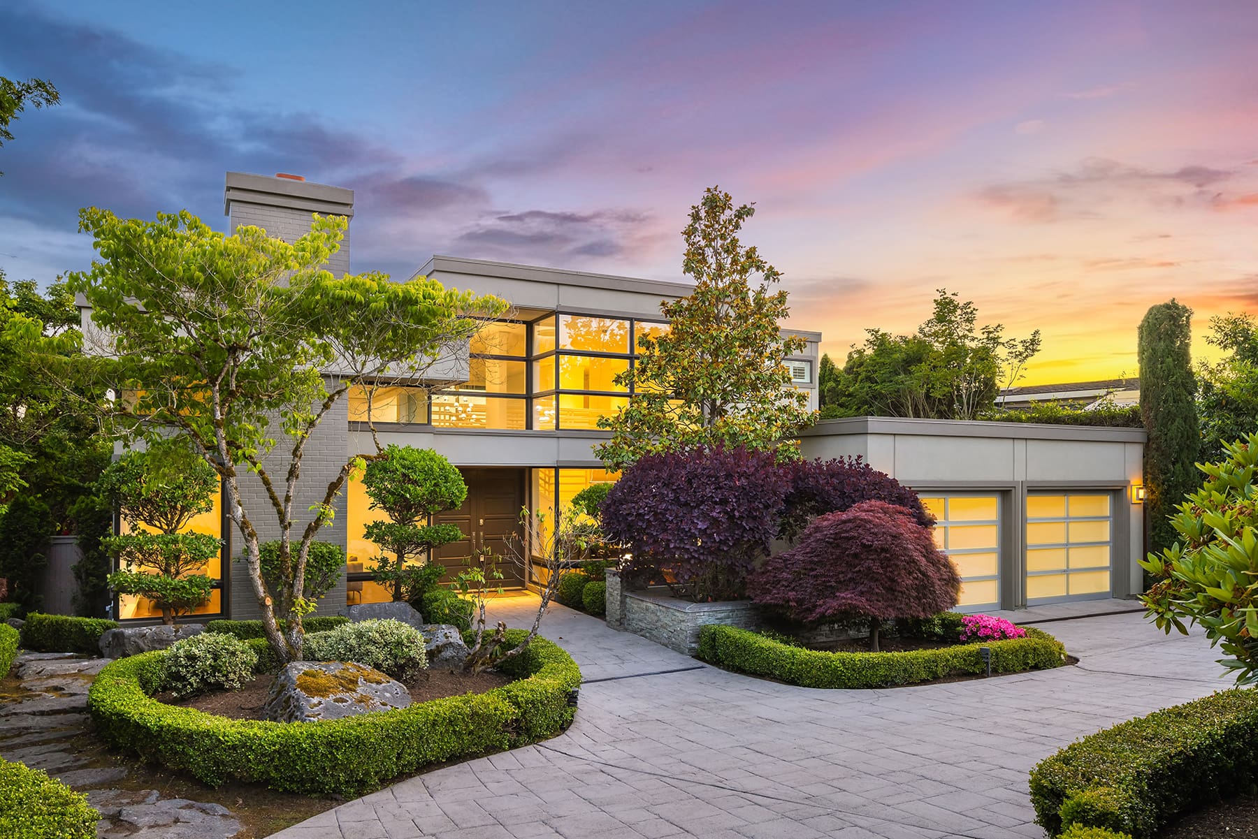 Modern exterior of a contemporary home at twilight, featuring large windows, lush landscaping, and a welcoming driveway, located in the Pacific Northwest.