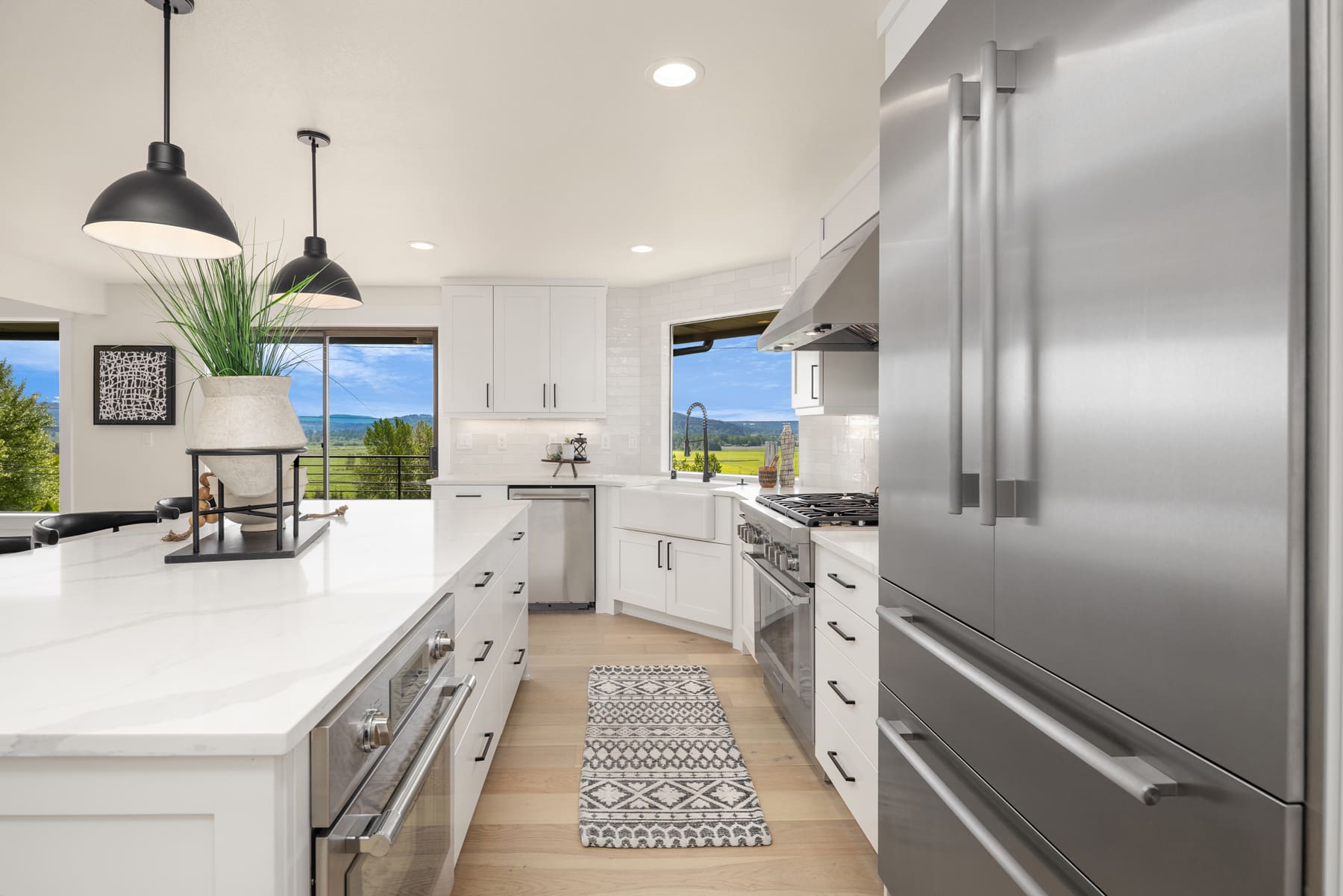 Modern kitchen featuring sleek white cabinetry, stainless steel appliances, and a spacious island with a marble countertop, set against picturesque views in the Pacific Northwest.
