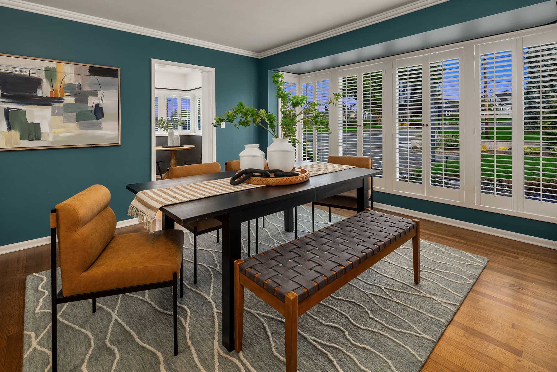 Modern dining room featuring a black dining table with stylish brown chairs and a woven bench, accented by a vibrant teal wall and natural light from large windows. Located in the Pacific Northwest.