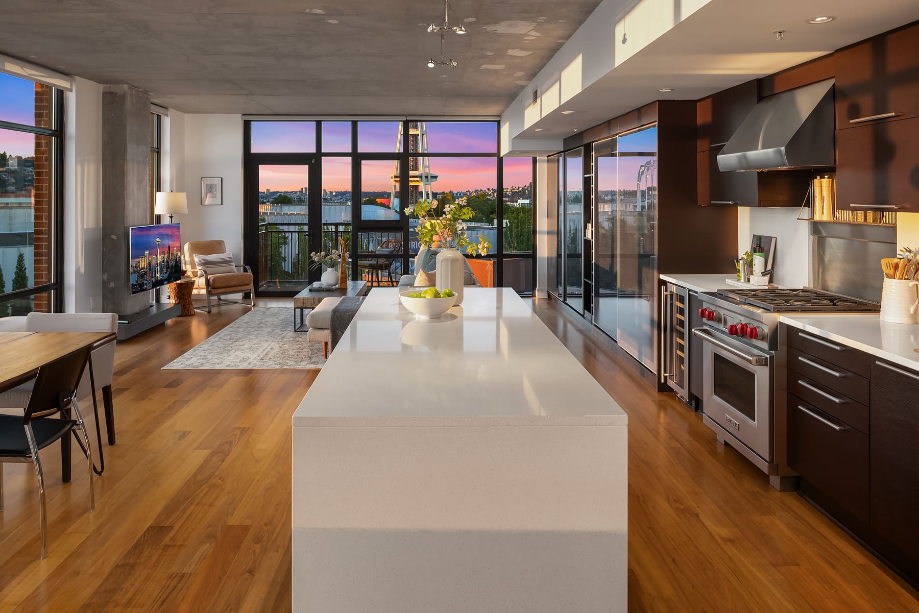 Modern kitchen and living space with elegant design features, showcasing a spacious island and large windows with a view of the Seattle skyline at twilight. Located in the Pacific Northwest.