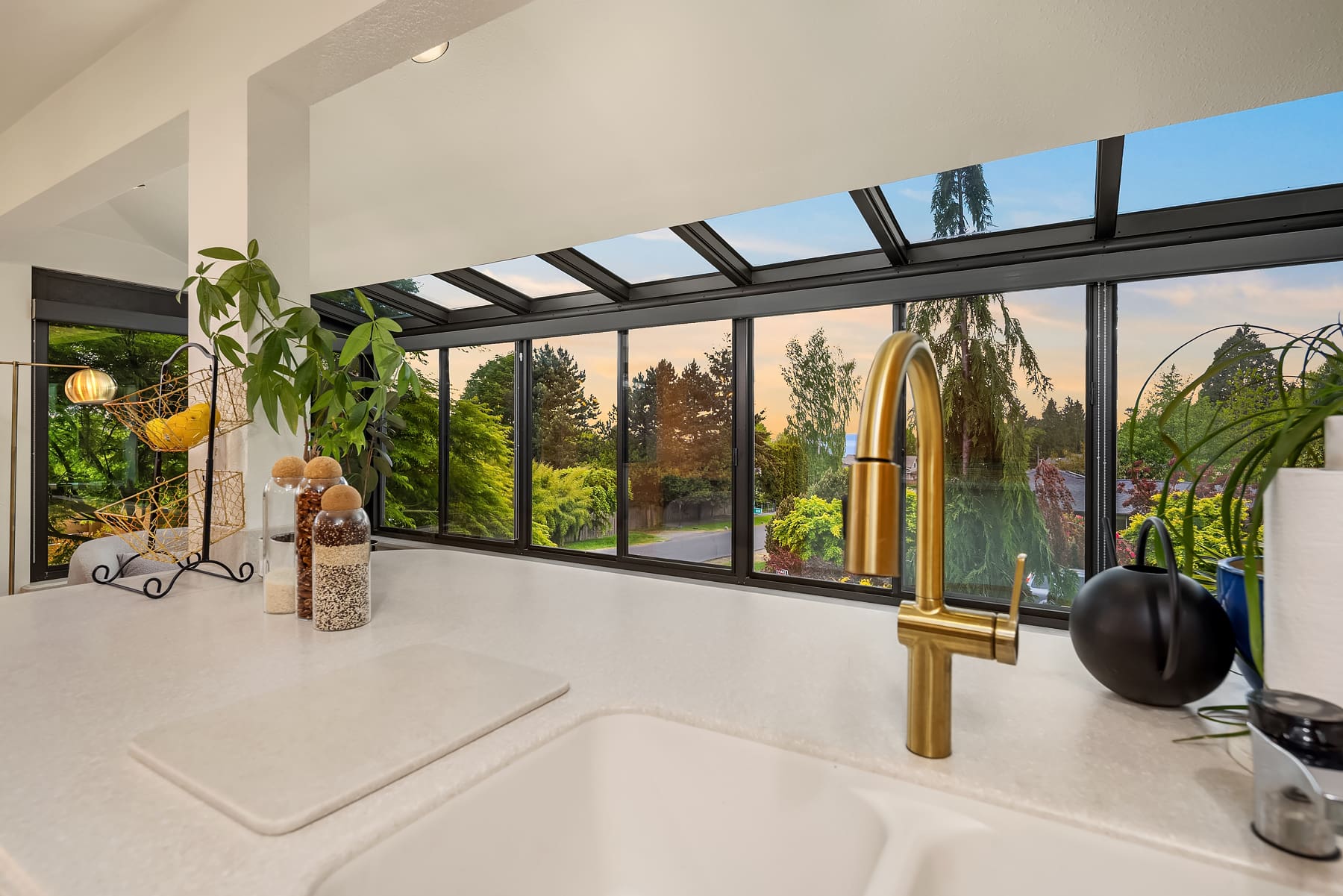 Modern kitchen with a sleek design featuring a golden faucet, large windows showcasing lush greenery, and a serene sunset view in the Pacific Northwest.