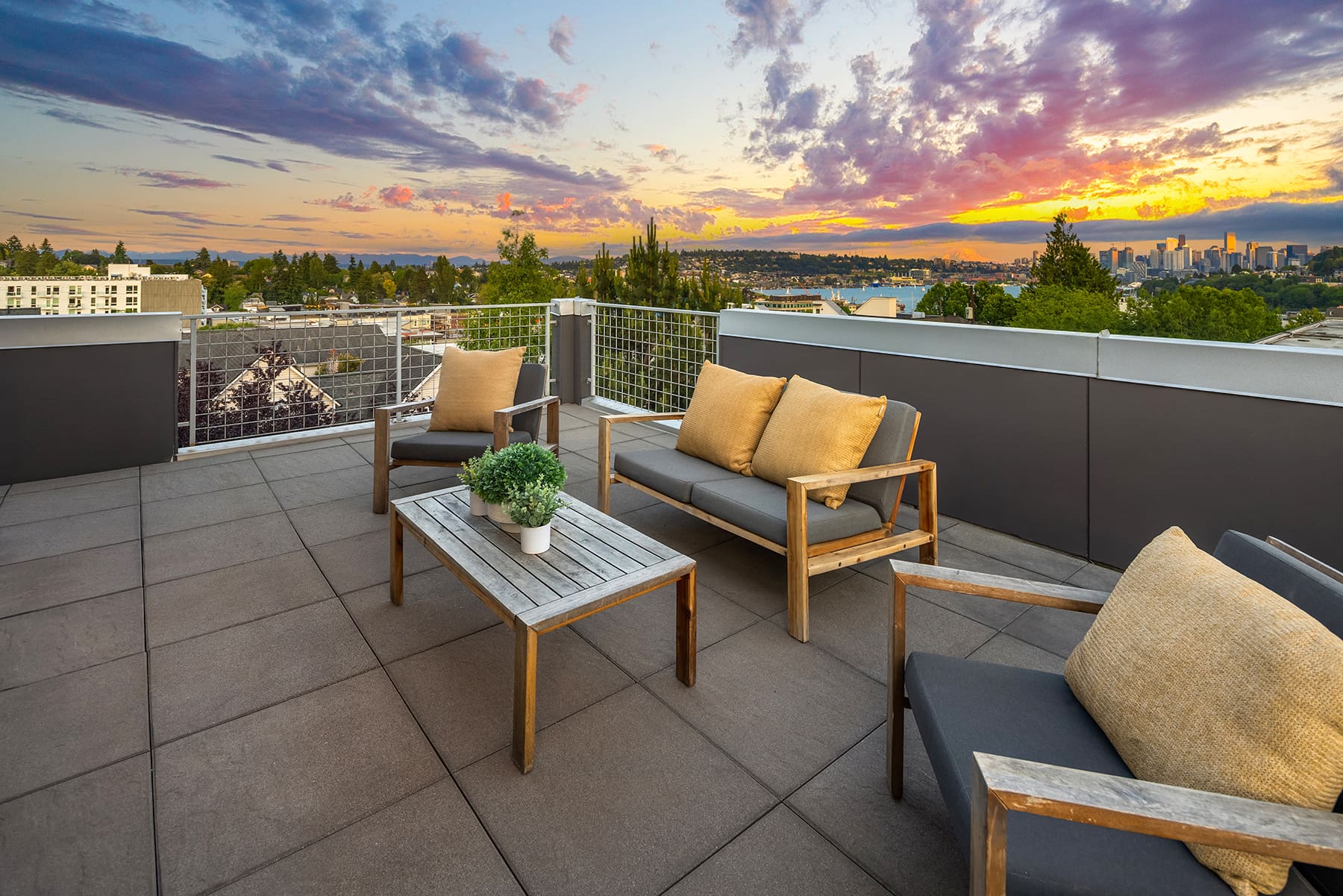 Rooftop terrace with modern seating and a wooden table, showcasing a stunning sunset view over Seattle's skyline and surrounding greenery.