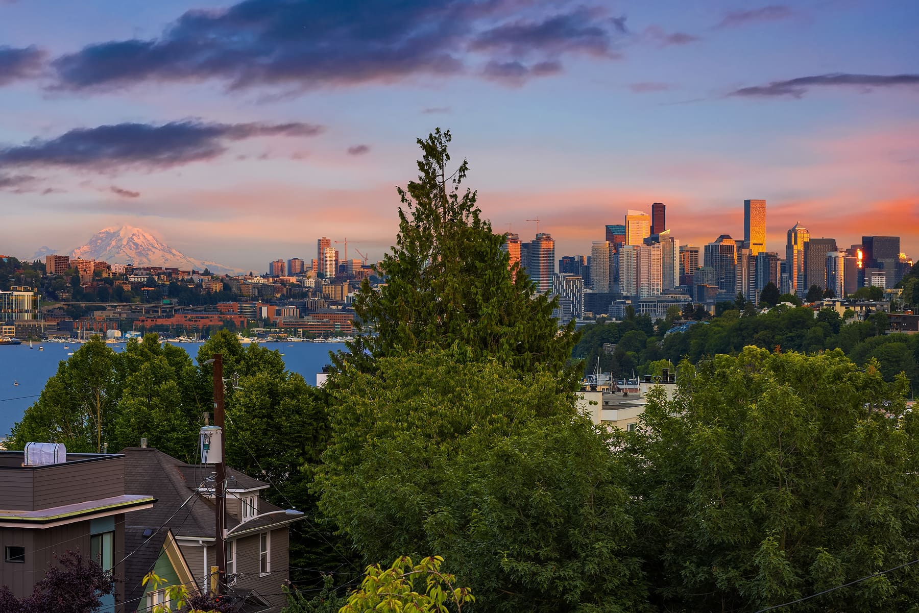 Stunning view of Seattle's skyline at twilight, featuring Mount Rainier in the background and lush greenery in the foreground, showcasing a vibrant blend of urban and natural beauty.