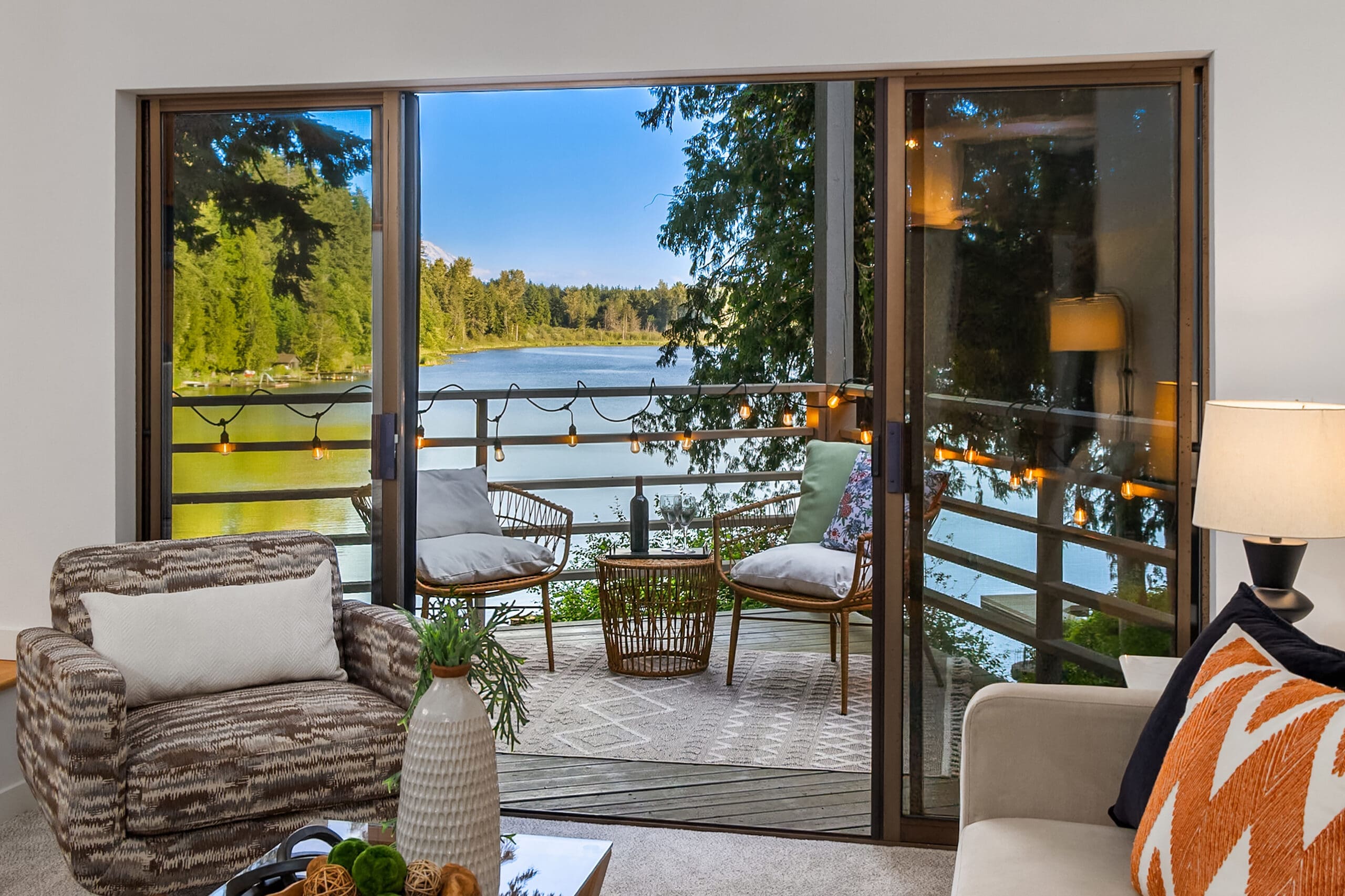 Cozy living room with modern decor featuring a plush armchair and stylish lamp, leading to a scenic balcony overlooking a tranquil lake in the Pacific Northwest.