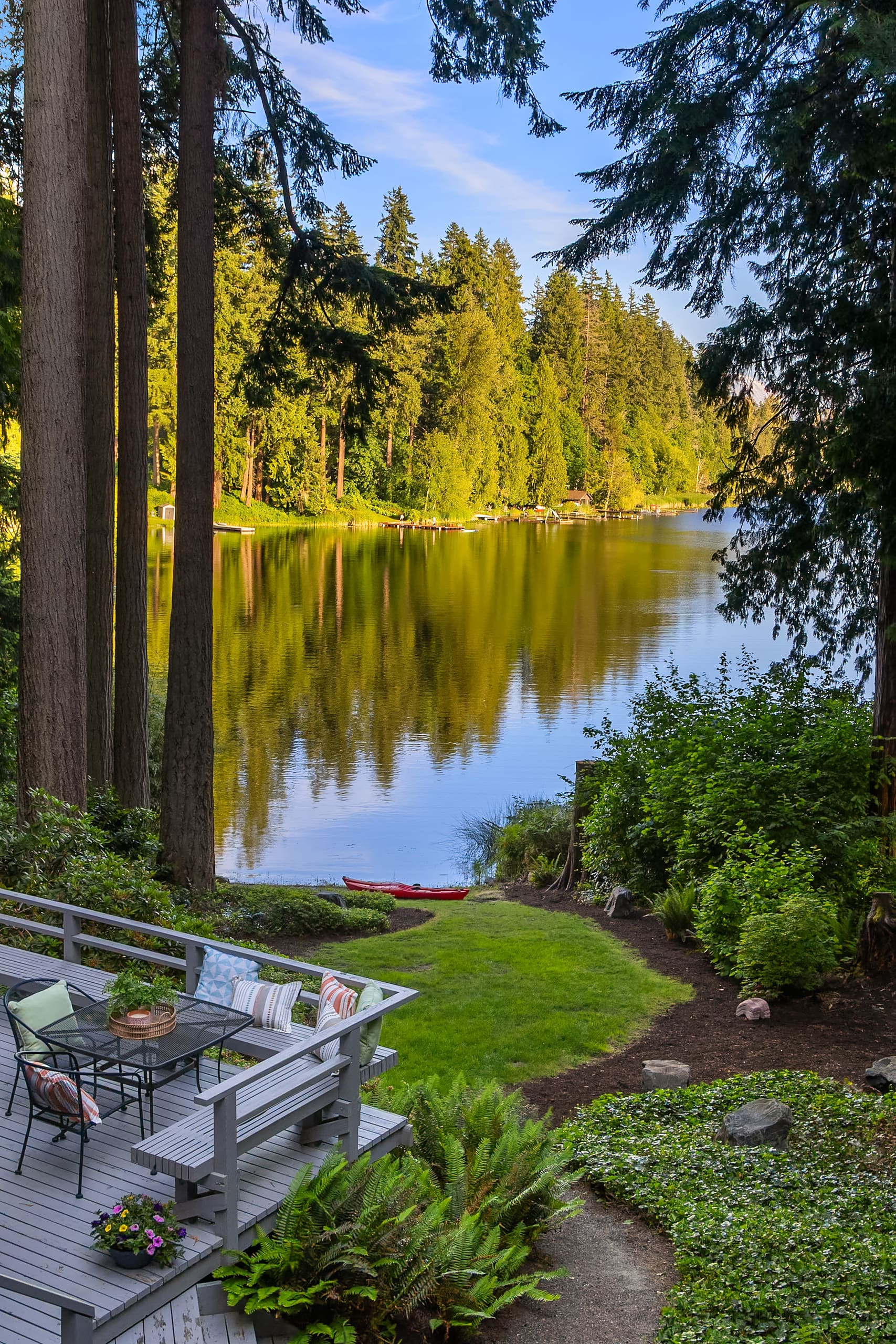 Serene waterfront deck with modern outdoor seating, surrounded by lush greenery and tall trees, reflecting a tranquil mood in the Pacific Northwest.