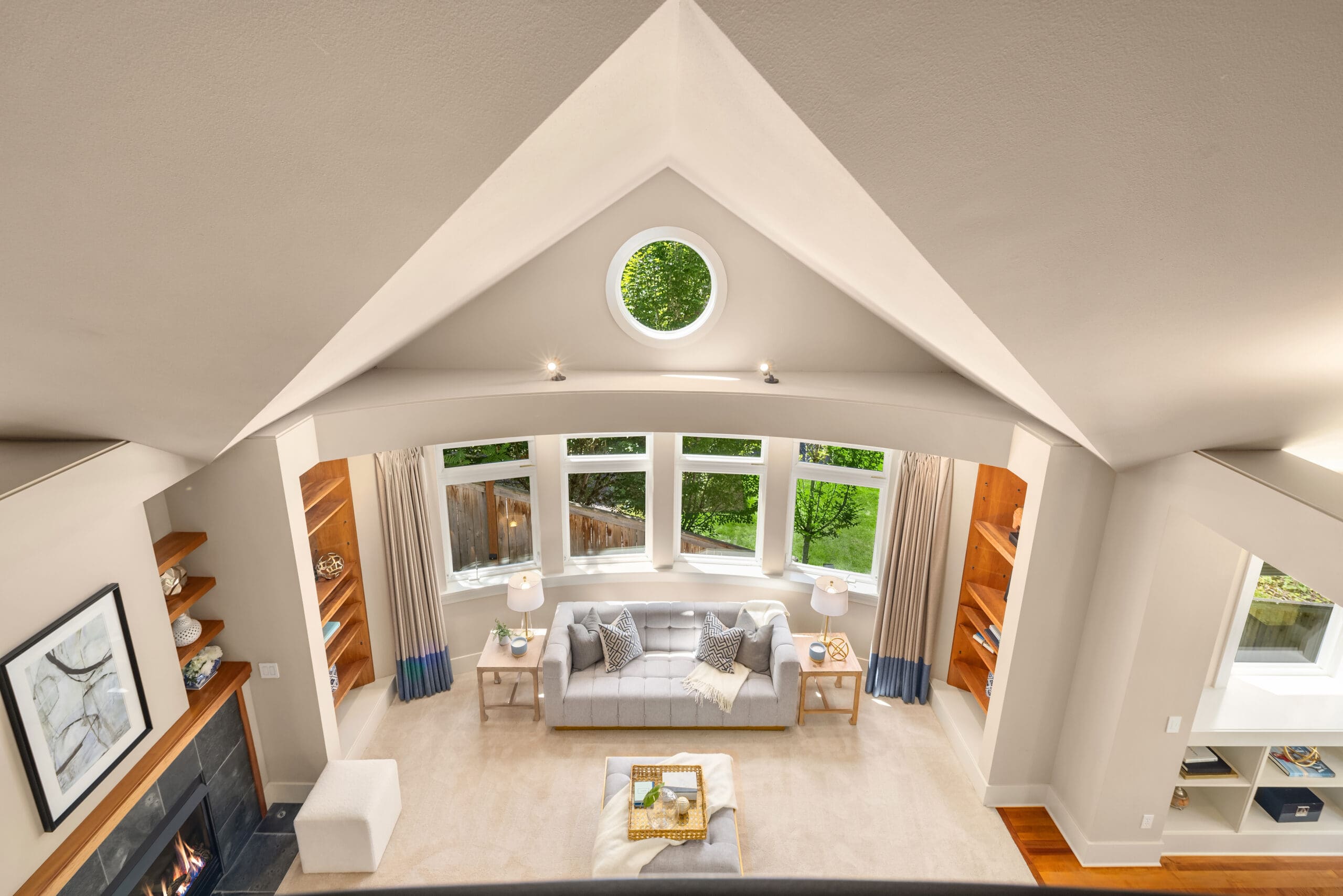 Spacious modern living room with vaulted ceiling and large bay windows, featuring elegant furnishings and a cozy fireplace, located in the Pacific Northwest.