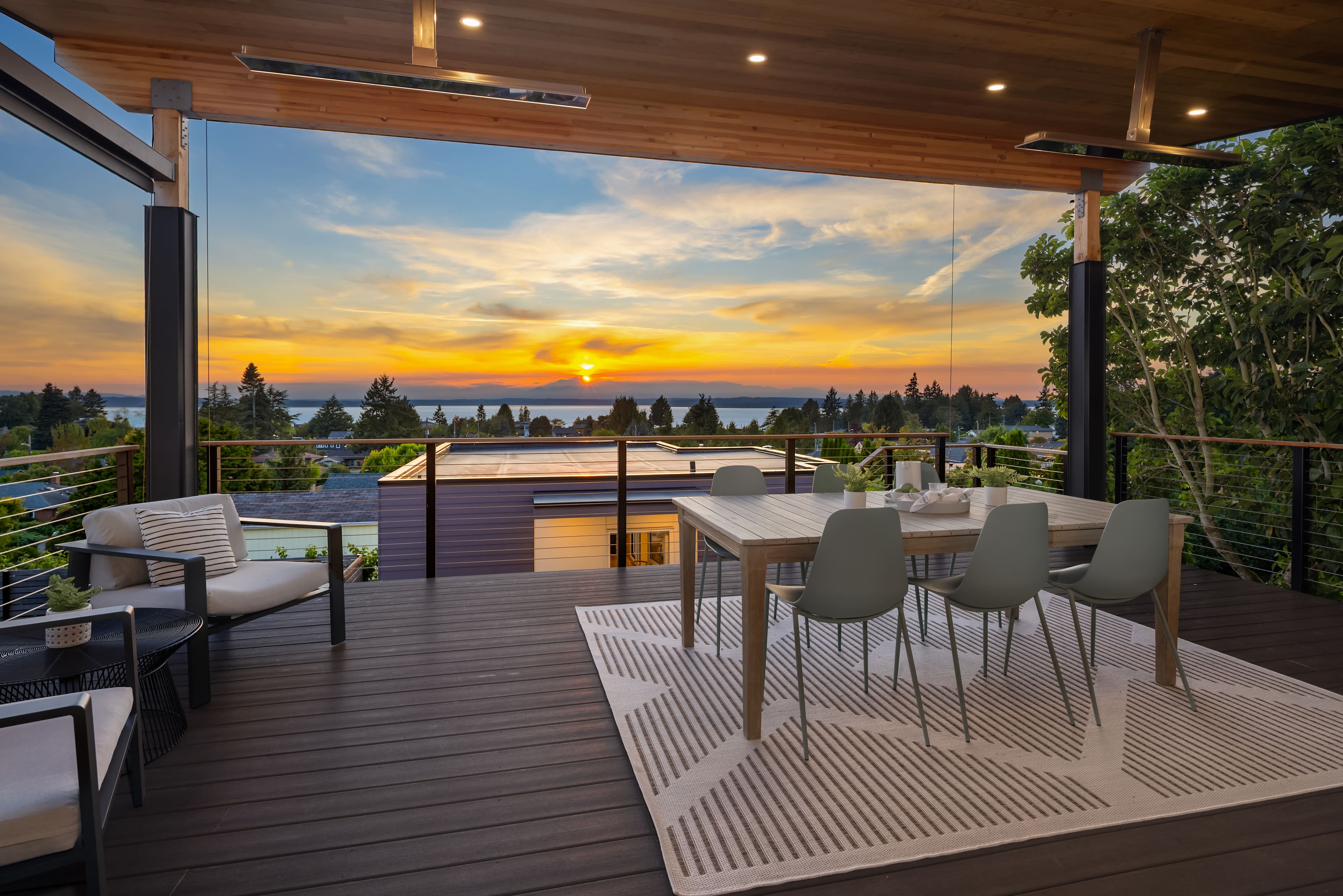 Stunning outdoor dining area with modern design, featuring a wooden table and sleek chairs, set against a breathtaking sunset view over the water in the Pacific Northwest.