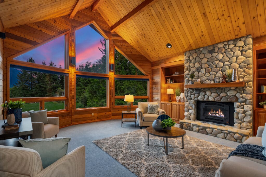 Casey Spring Seattle photographer. Cozy living room featuring a stone fireplace and large windows showcasing a twilight view, designed with warm wooden accents and plush furnishings, located in the Pacific Northwest.