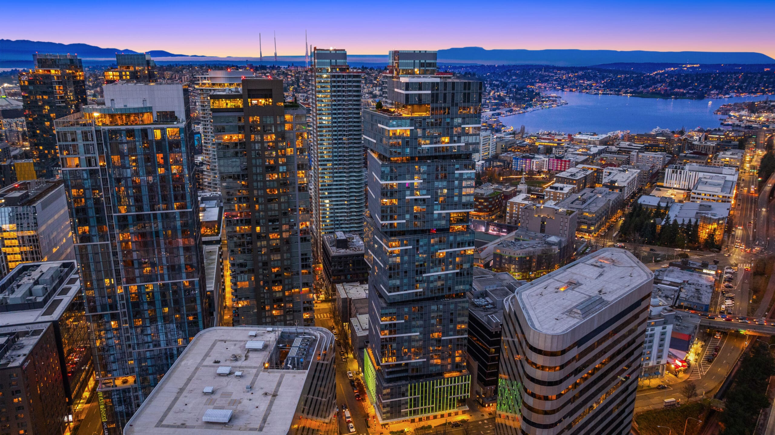 Aerial view of Seattle's vibrant skyline at twilight, showcasing modern high-rise buildings illuminated against a backdrop of the water and mountains.