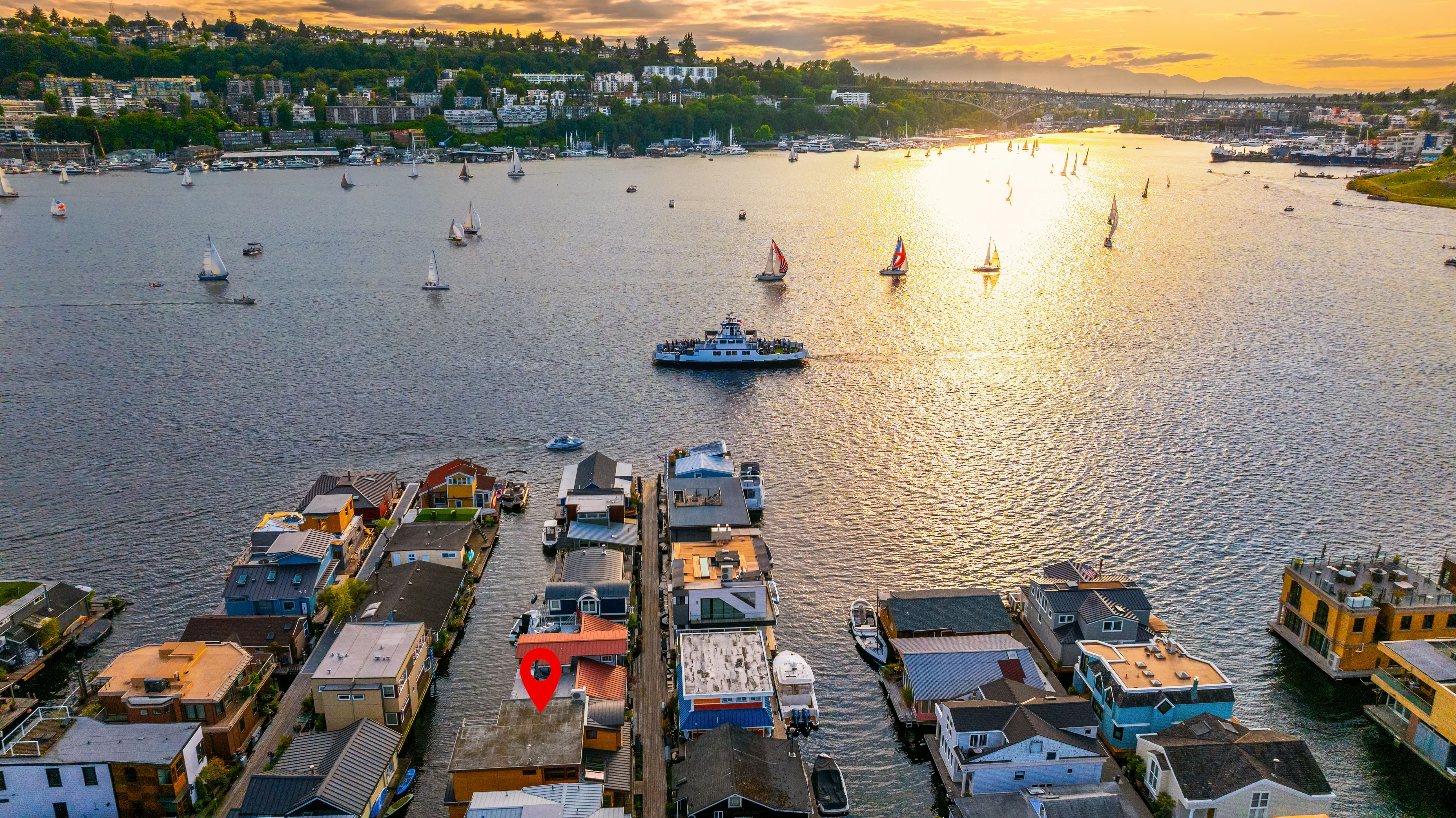 Aerial view of floating homes on the water at sunset in Seattle, showcasing vibrant sailboats and a scenic waterfront landscape.