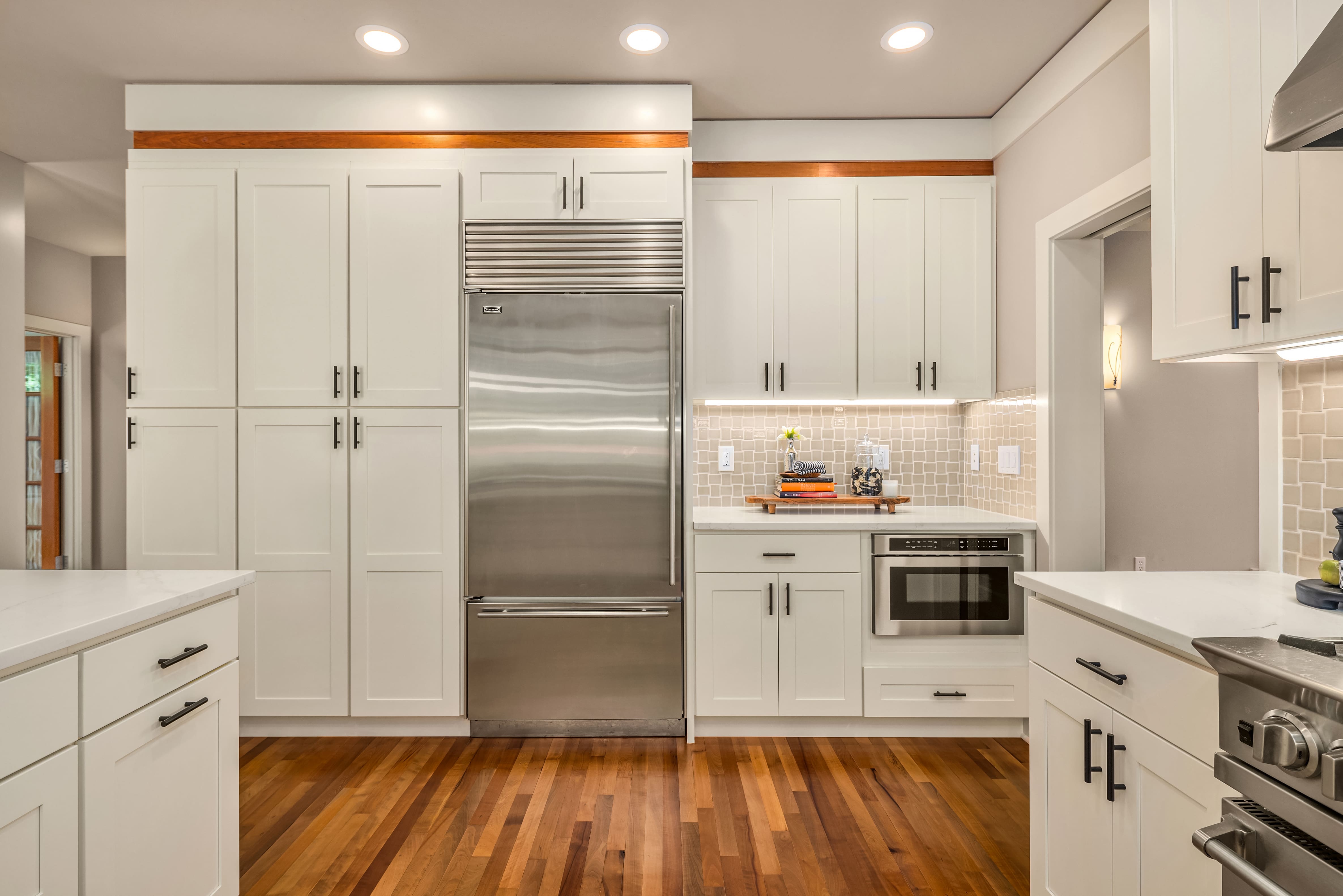 Modern kitchen featuring sleek white cabinetry, stainless steel appliances, and warm wood flooring, located in the Pacific Northwest.