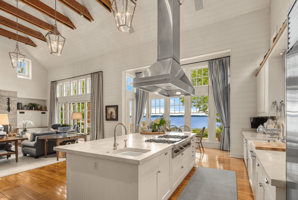 Modern kitchen with high ceilings, exposed wooden beams, and large windows showcasing waterfront views, located in the Pacific Northwest.
