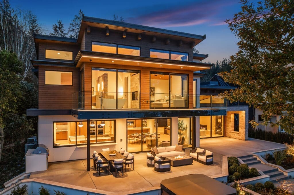 Modern luxury home exterior with large glass windows, showcasing a stylish outdoor seating area and fire pit, set against a twilight sky in the Pacific Northwest.